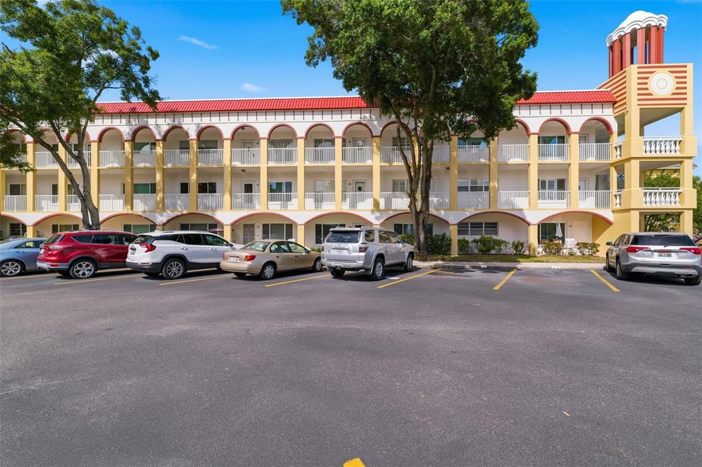 A three-story apartment building with arched balconies and a parking lot in the foreground — 2430 FLORENTINE WAY UNIT 58, CLEARWATER, FL