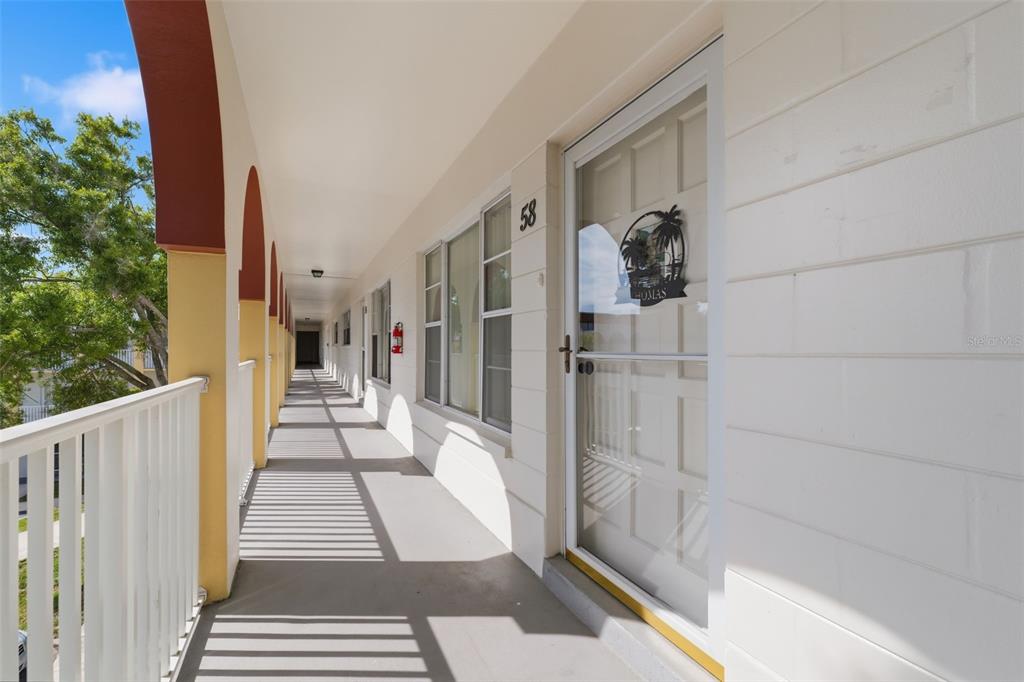 An exterior walkway with white railings and arched columns leads to a residential unit door — 2430 FLORENTINE WAY UNIT 58, CLEARWATER, FL