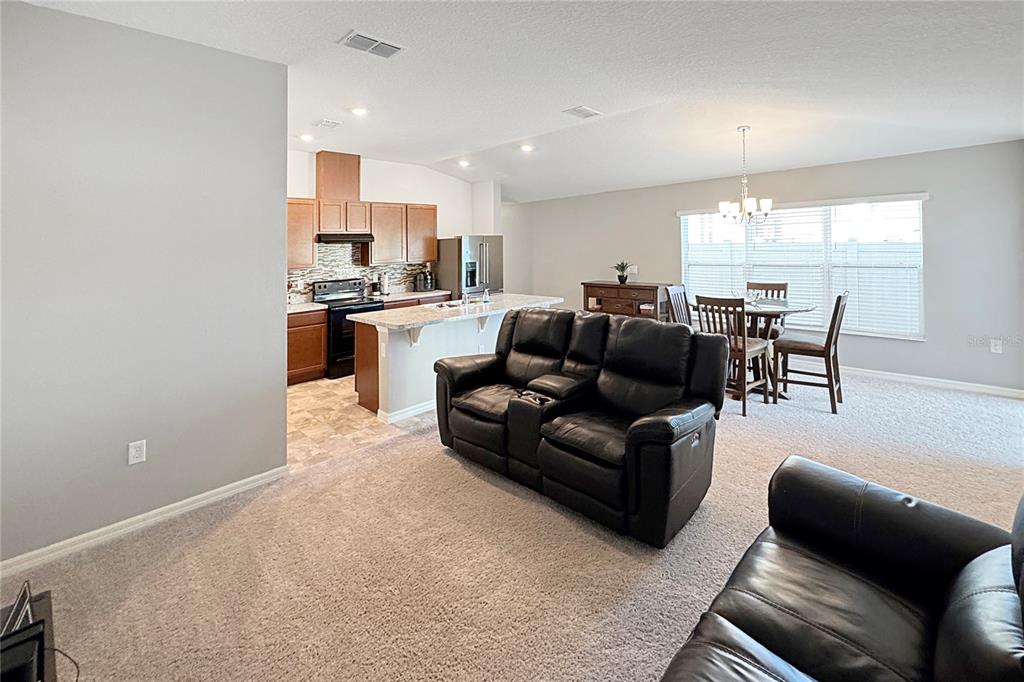 An open-concept living room and kitchen featuring a black leather sofa and wooden cabinets — 591 PRESERVE POINTE BOULEVARD, DAVENPORT, FL