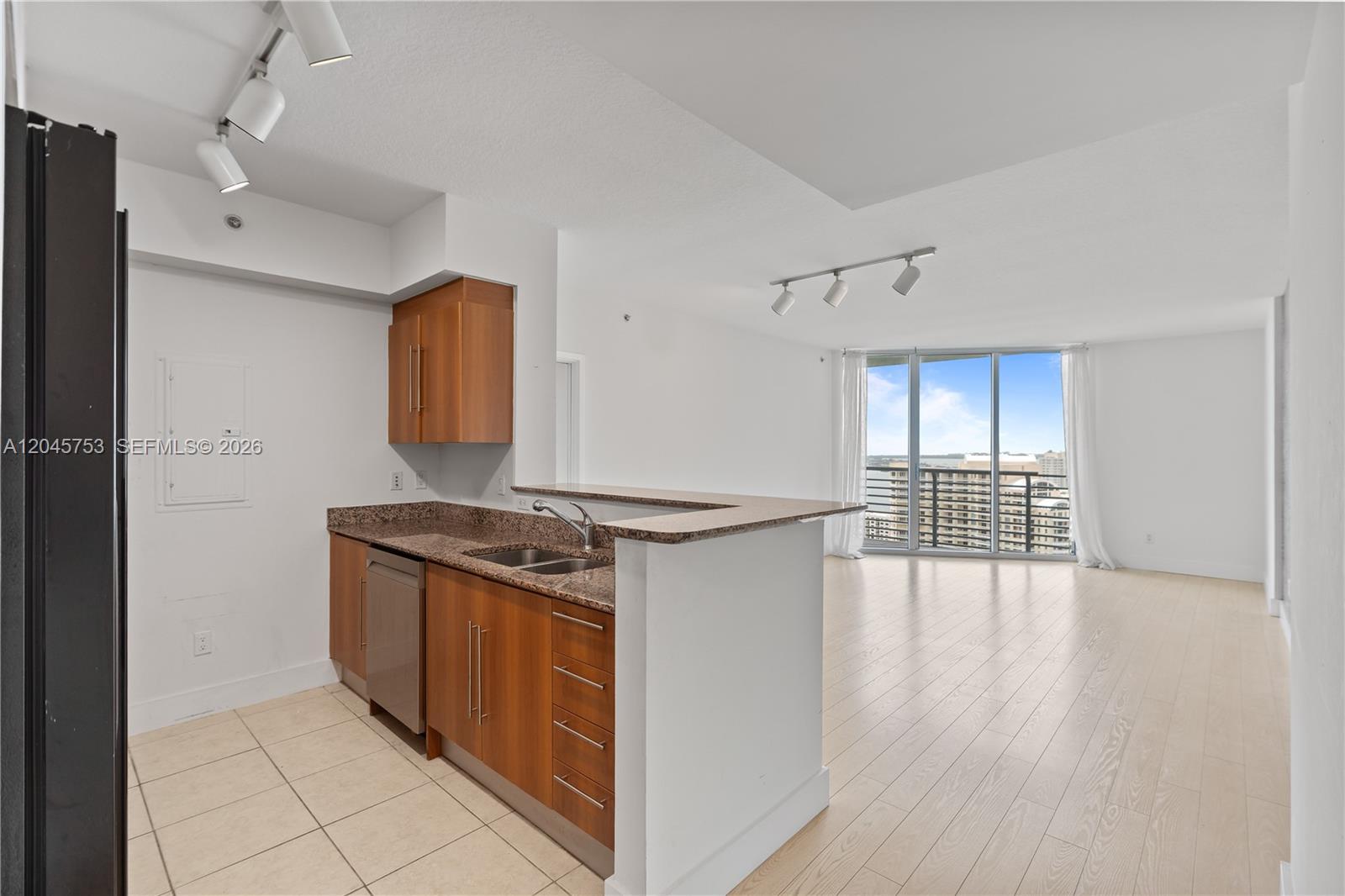 A kitchen with wood cabinets and granite countertops opens into a bright living area — 335 S Biscayne Blvd # 3503, Miami FL 33131, MIAMI, FL