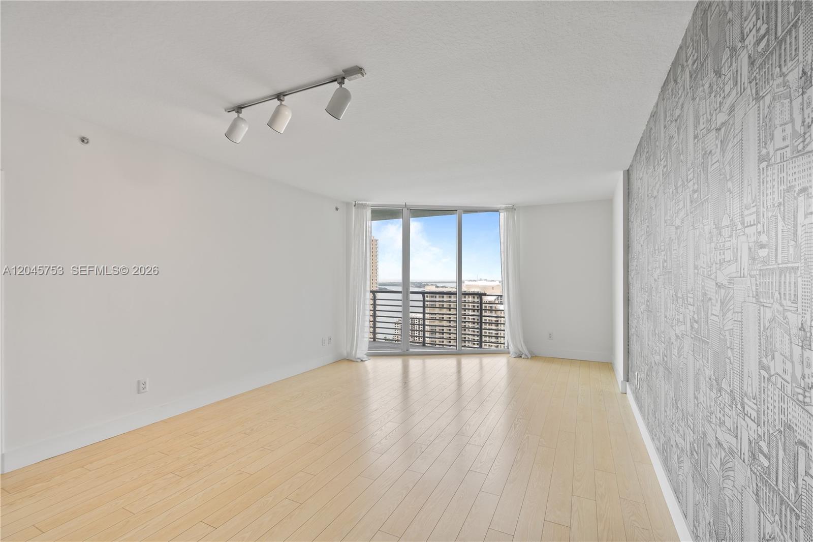 An empty room features light wood flooring, a patterned accent wall, and a balcony view — 335 S Biscayne Blvd # 3503, Miami FL 33131, MIAMI, FL