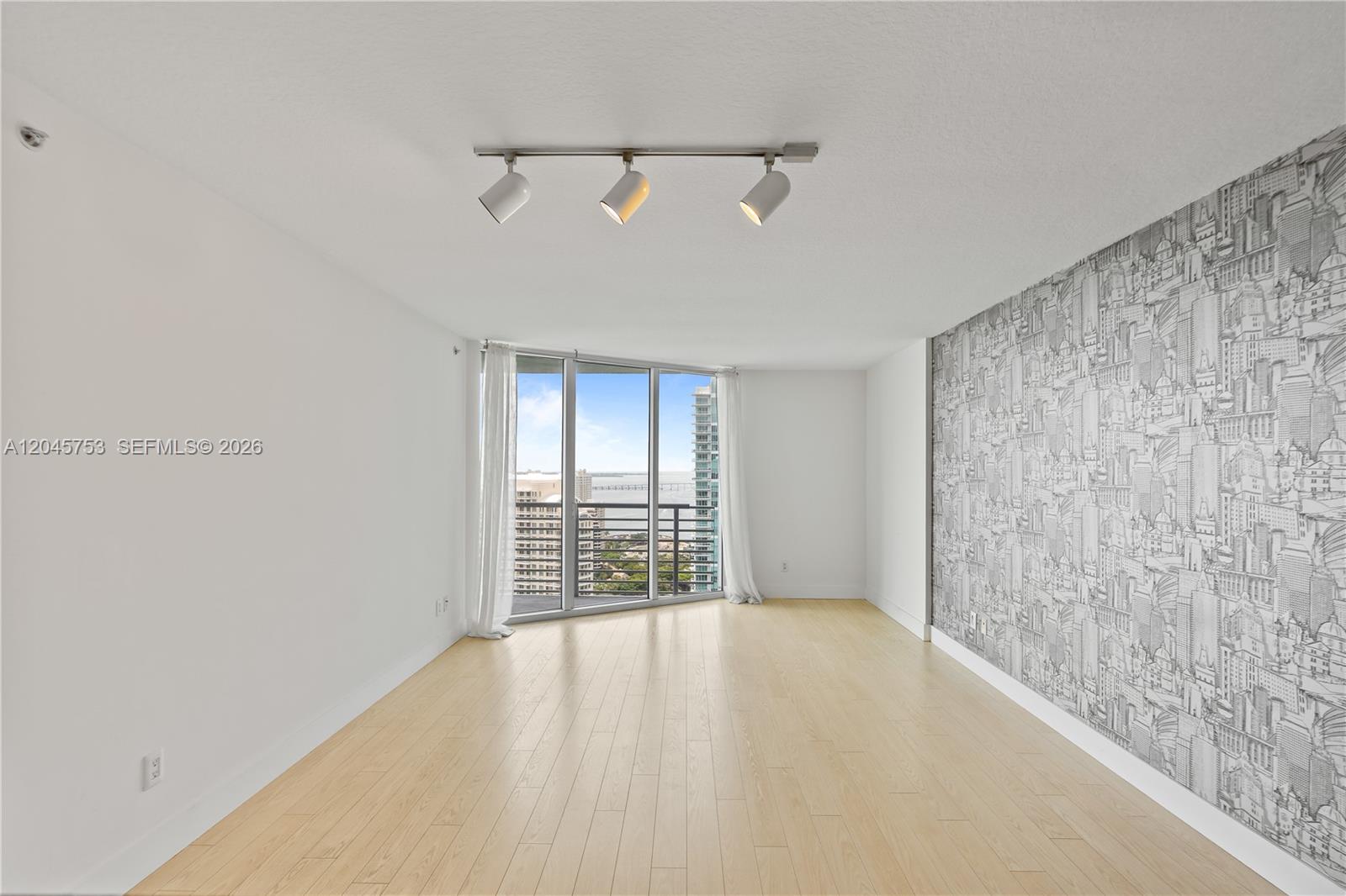 A bright living room features light wood flooring, a patterned accent wall, and floor-to-ceiling windows — 335 S Biscayne Blvd # 3503, Miami FL 33131, MIAMI, FL