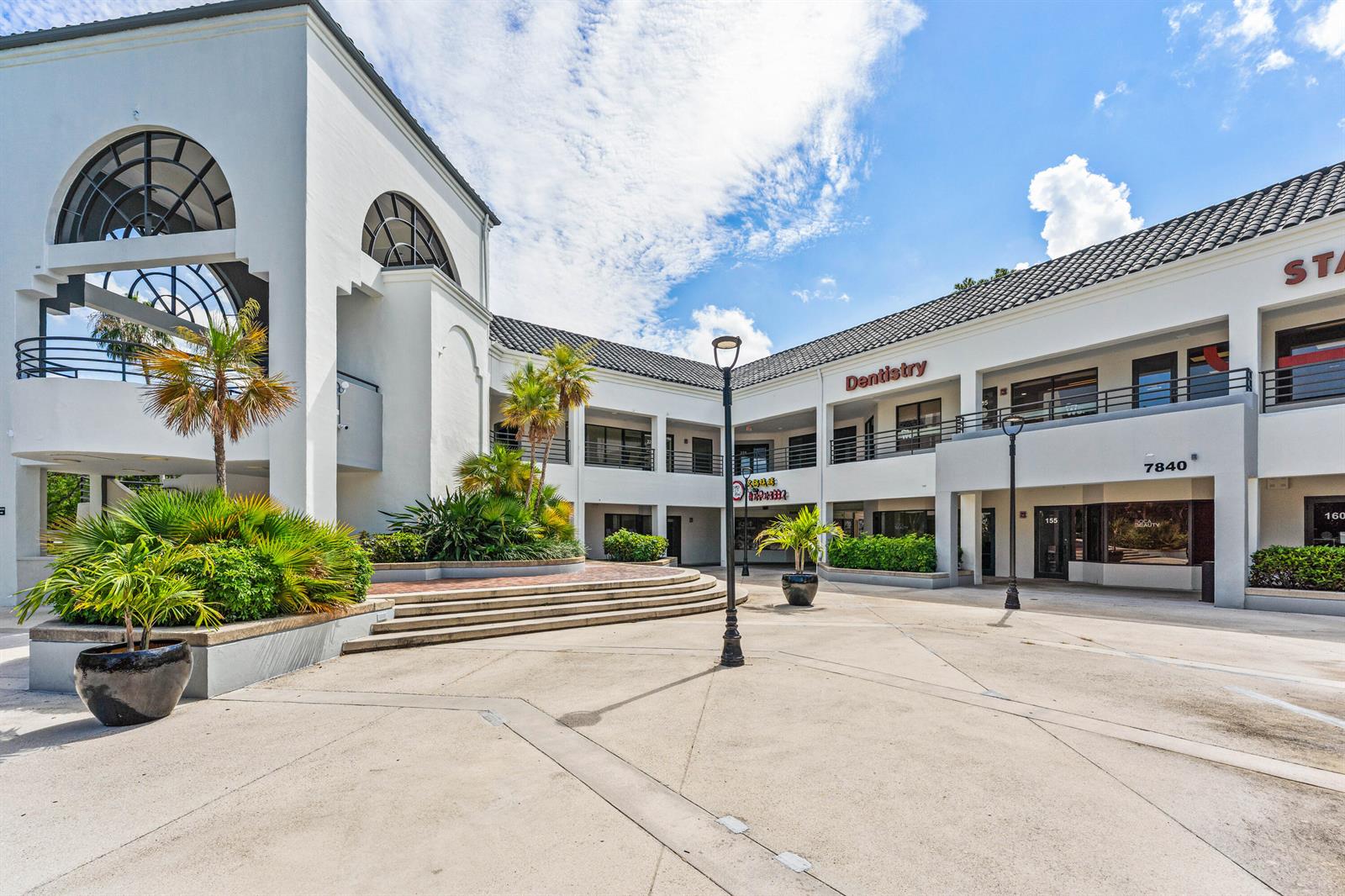 An exterior view of a two-story commercial plaza with white stucco walls and palm trees — 7880 Glades Road, Boca Raton FL 33434, BOCA RATON, FL