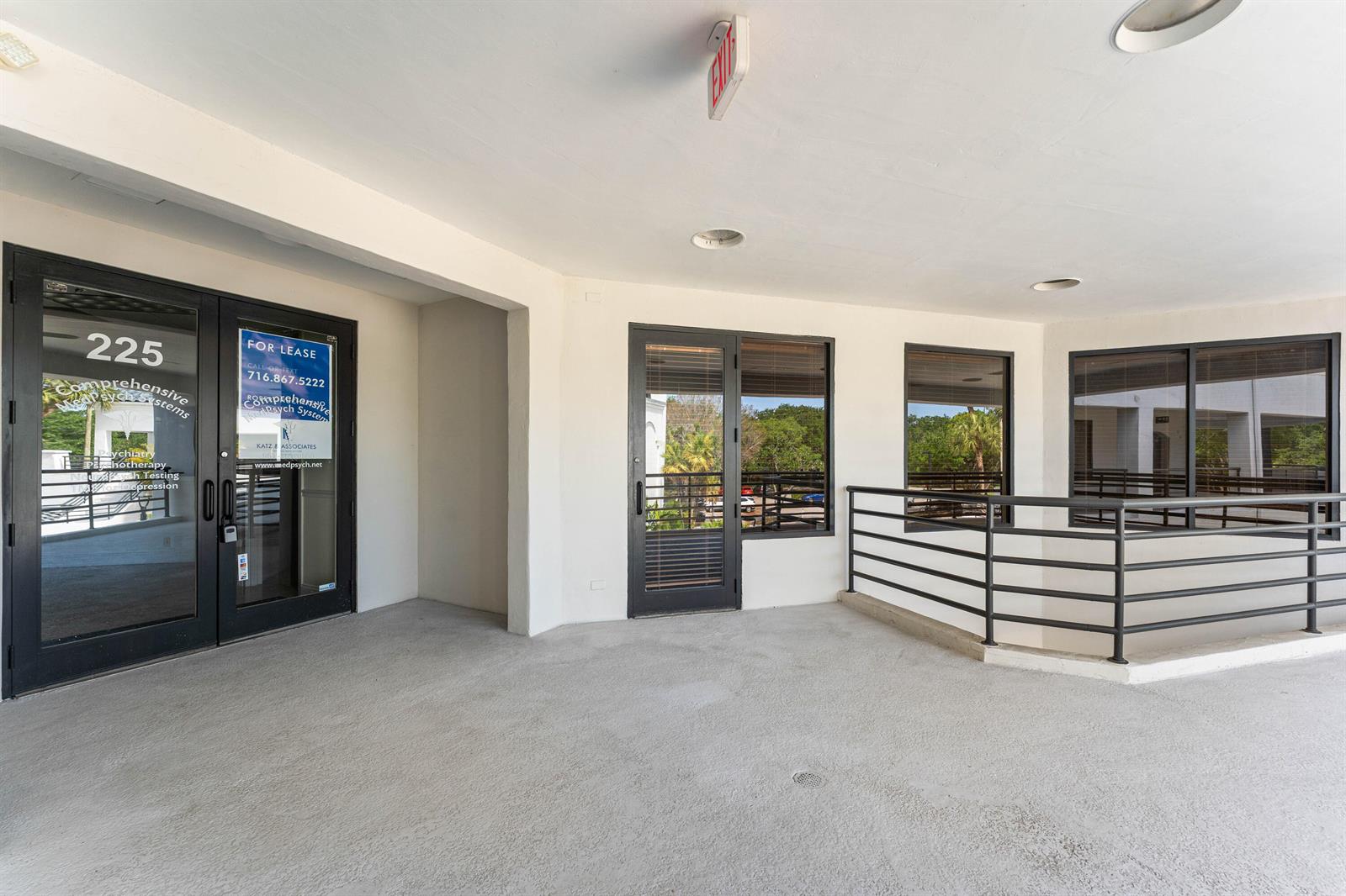 An outdoor covered walkway features glass doors, a black metal railing, and concrete flooring — 7880 Glades Road, Boca Raton FL 33434, BOCA RATON, FL