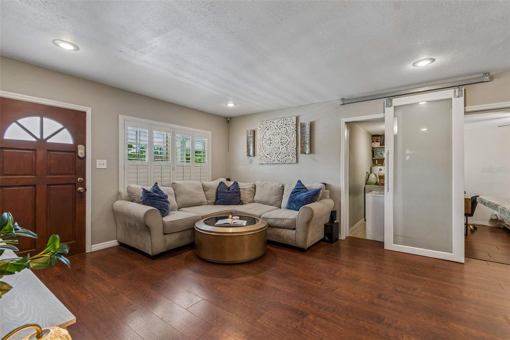 A living room features a sectional sofa, dark wood flooring, and a sliding glass door — 11307 N BOULEVARD, TAMPA, FL