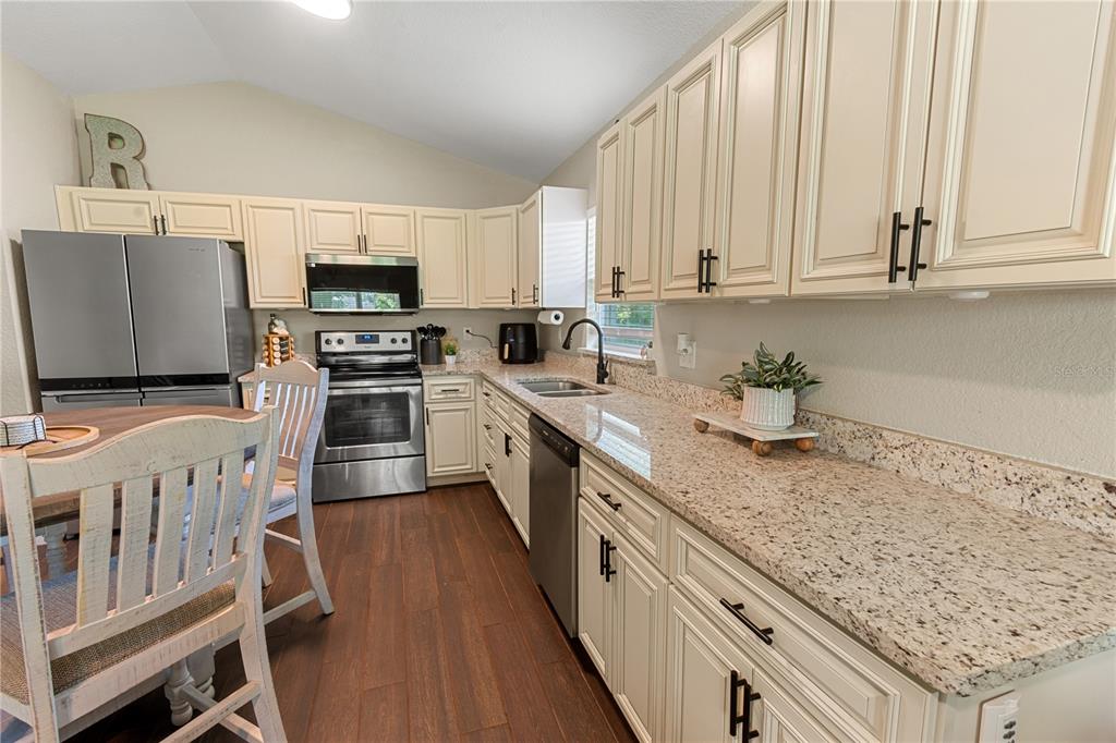 A kitchen features cream-colored cabinets, granite countertops, stainless steel appliances, and wood-look flooring — 765 S DUDLEY AVENUE, BARTOW, FL