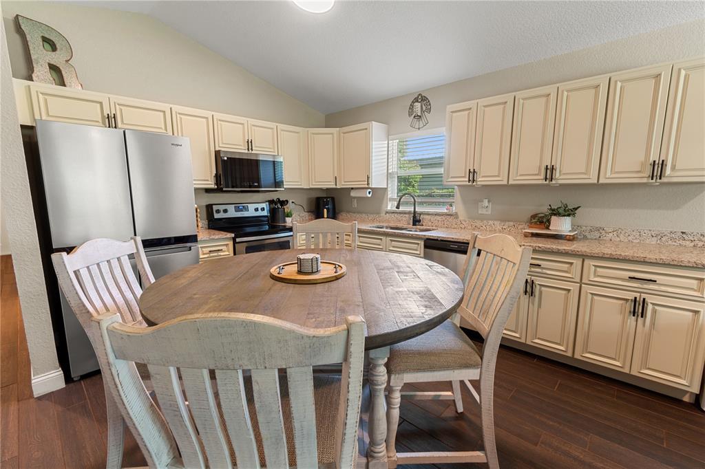 A kitchen features cream cabinets, granite countertops, stainless steel appliances, and a round wooden table — 765 S DUDLEY AVENUE, BARTOW, FL