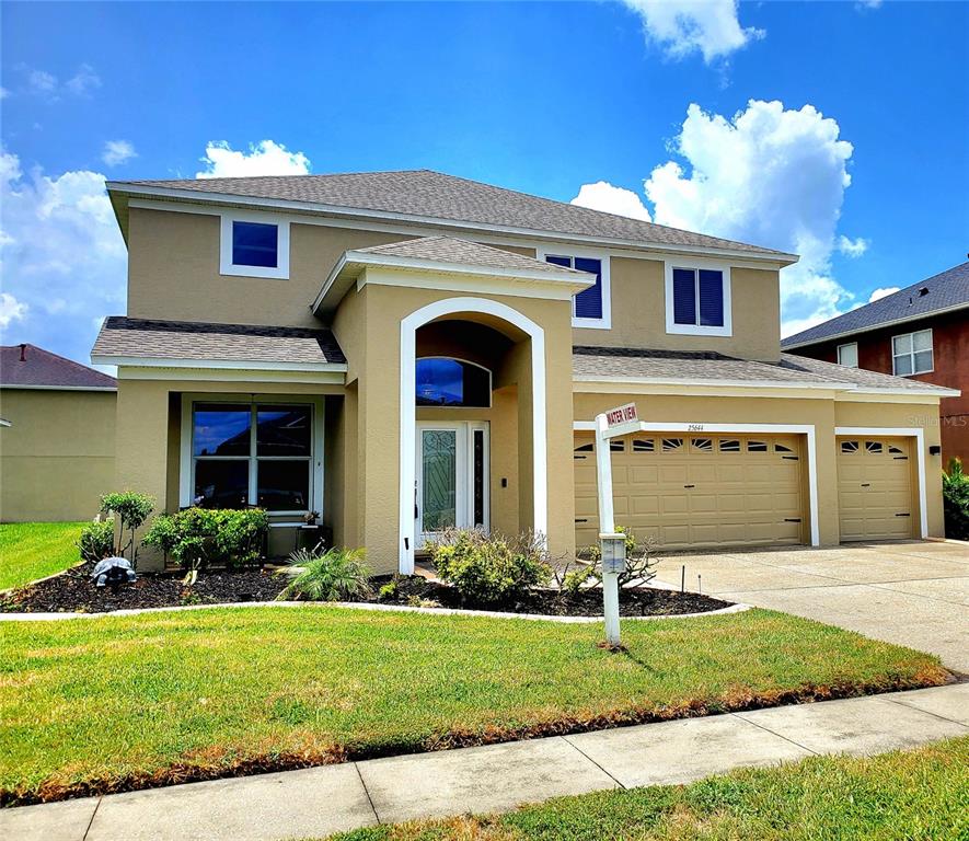 A two-story suburban house with a tan exterior, a three-car garage, and a front lawn — 25644 FRITH STREET, LAND O LAKES, FL