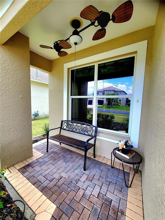 A covered patio features a brick floor, a metal bench, a small table, and a ceiling fan — 25644 FRITH STREET, LAND O LAKES, FL