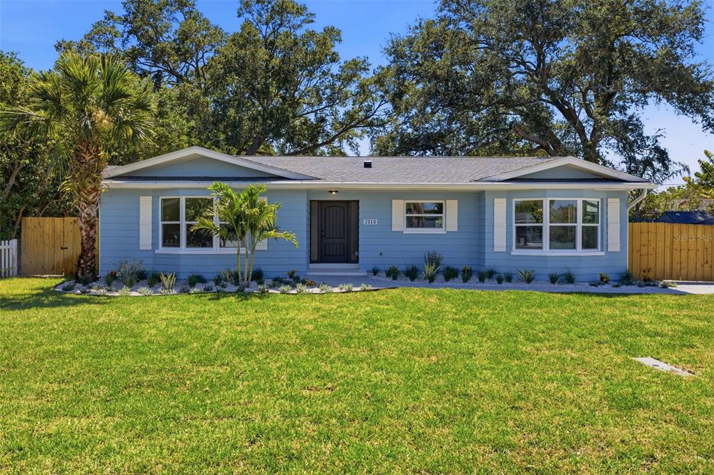 A light blue single-story house with white trim, a dark front door, and a grassy lawn — 2310 HARRISON DRIVE, DUNEDIN, FL