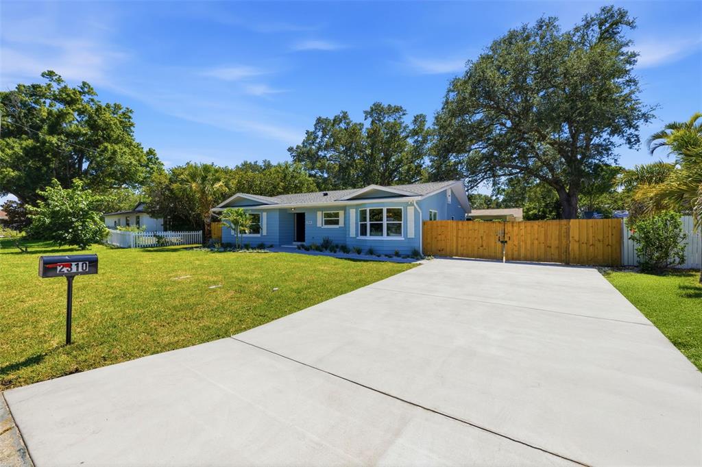 A blue single-story house with a concrete driveway and a wooden fence in the yard — 2310 HARRISON DRIVE, DUNEDIN, FL