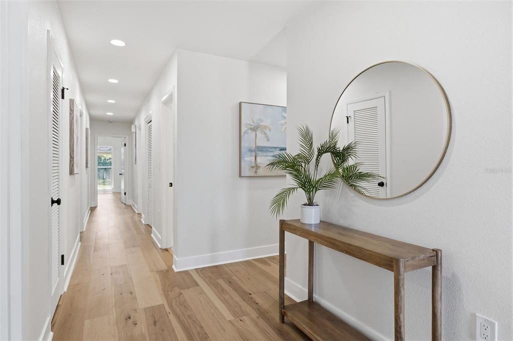 A bright hallway features light wood flooring, white walls, a console table, and a round mirror — 2310 HARRISON DRIVE, DUNEDIN, FL