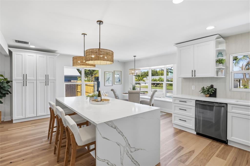 A bright kitchen features a large marble-topped island, white cabinetry, and light wood flooring — 2310 HARRISON DRIVE, DUNEDIN, FL
