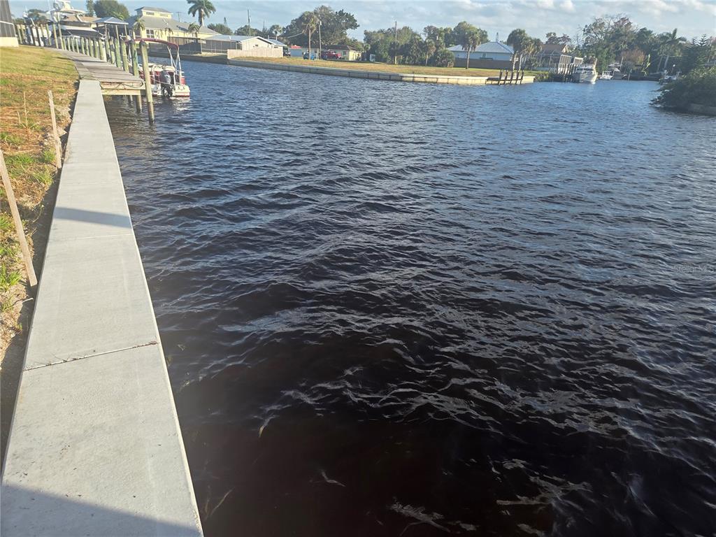 A concrete seawall borders a canal with a boat docked at a wooden pier — 13429 MARQUETTE BOULEVARD, FORT MYERS, FL