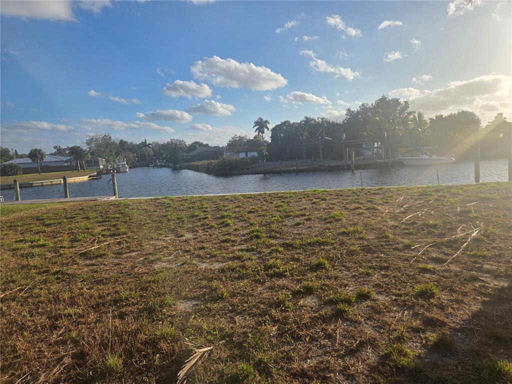 A vacant waterfront lot features a grassy foreground and a view of a canal — 13429 MARQUETTE BOULEVARD, FORT MYERS, FL