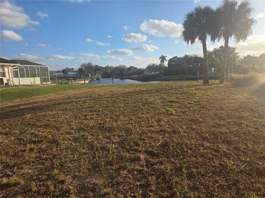 A grassy vacant lot overlooks a canal with palm trees and neighboring houses in view — 13429 MARQUETTE BOULEVARD, FORT MYERS, FL