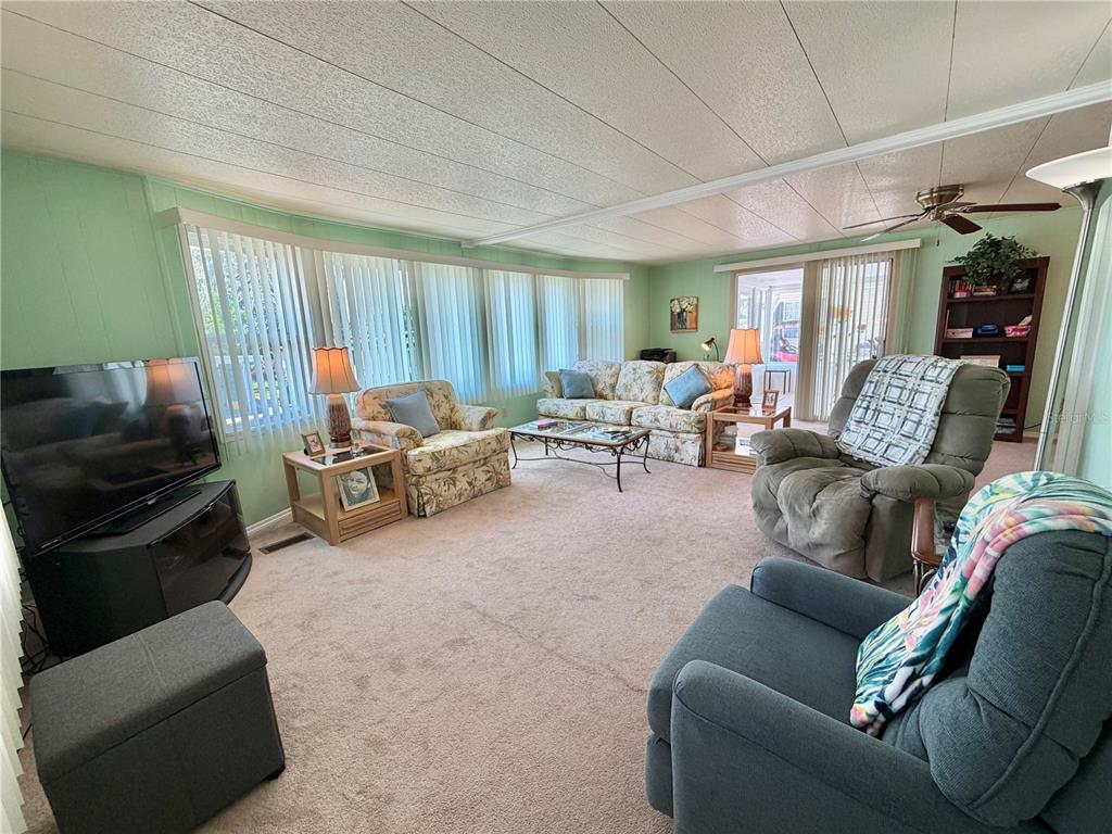 A living room with light green walls, carpeted flooring, a sofa, and several armchairs — 114 ASPEN CIRCLE, LEESBURG, FL