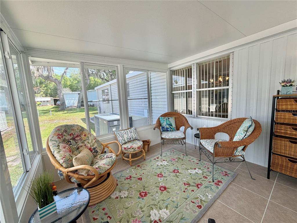 A sunroom with tiled floors, wicker furniture, and large windows overlooking a grassy yard — 114 ASPEN CIRCLE, LEESBURG, FL
