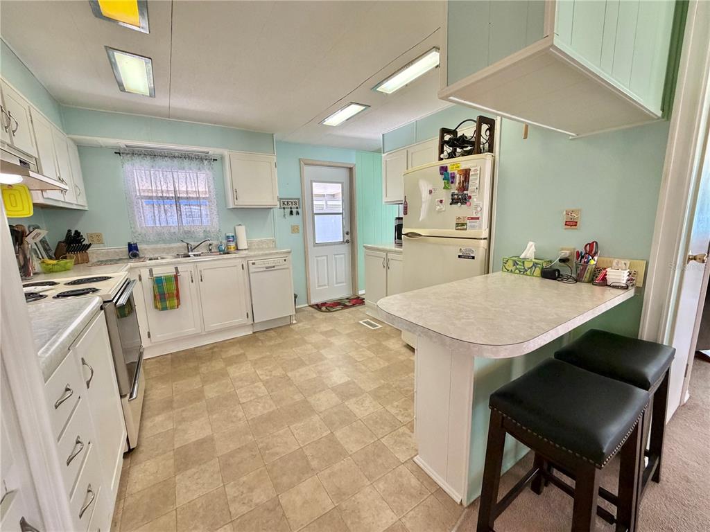 A kitchen with white cabinets, light blue walls, a breakfast bar, and vinyl flooring — 114 ASPEN CIRCLE, LEESBURG, FL