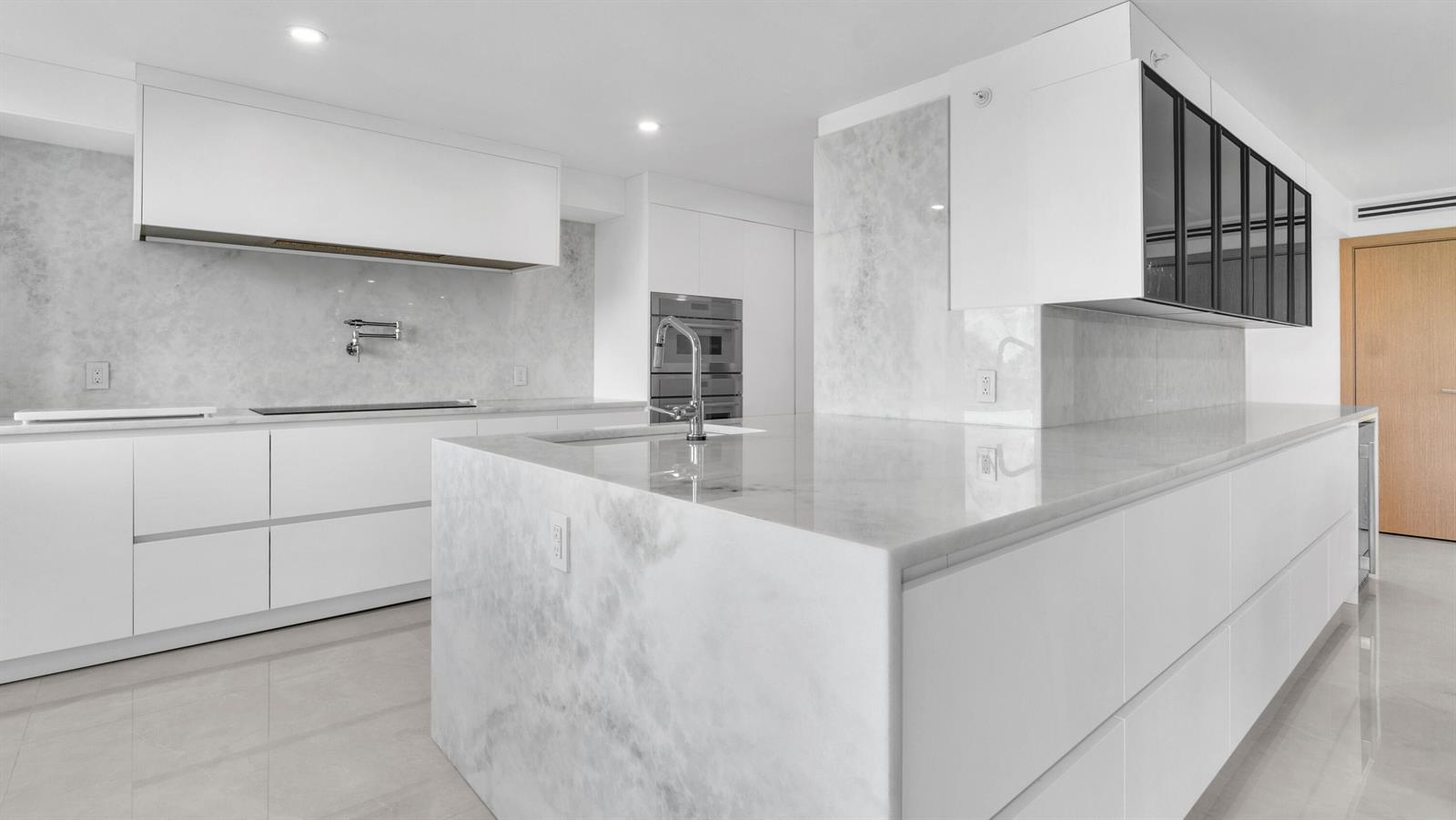 A modern kitchen features white cabinetry, a large marble island, and marble slab backsplashes — 901 E Camino Real # 2a, Boca Raton FL 33432, BOCA RATON, FL