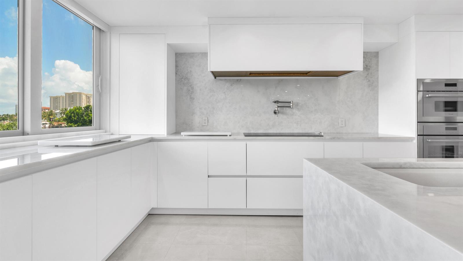 A modern white kitchen features marble countertops, a wall-mounted pot filler, and a large window — 901 E Camino Real # 2a, Boca Raton FL 33432, BOCA RATON, FL