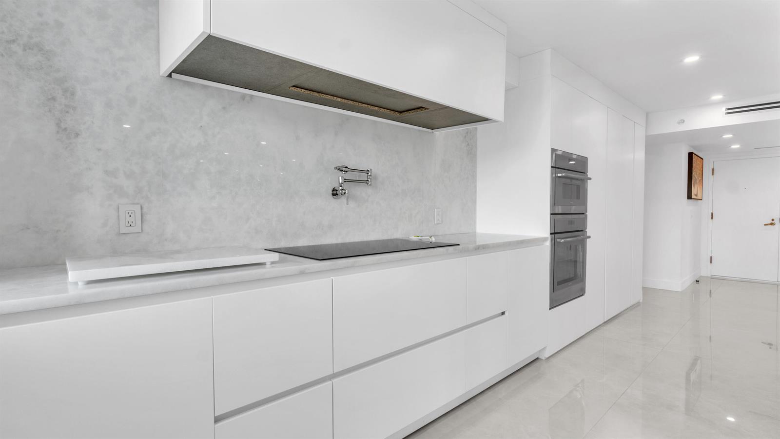 A modern white kitchen features marble countertops, a wall-mounted pot filler, and built-in appliances — 901 E Camino Real # 2a, Boca Raton FL 33432, BOCA RATON, FL