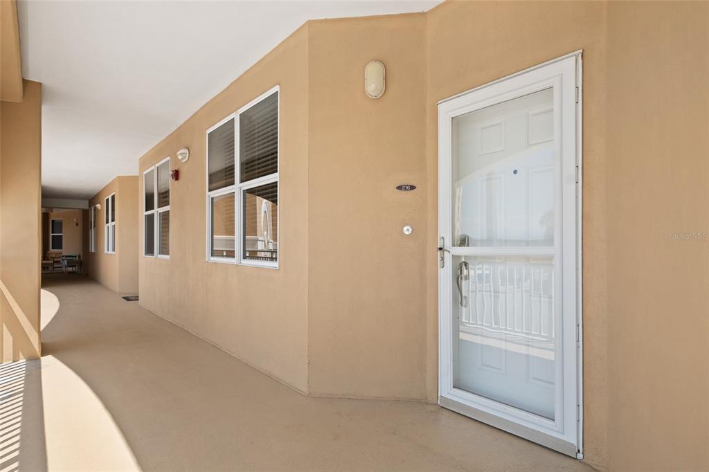 An exterior view of a tan building hallway featuring a white door and windows — 80 SURFVIEW DRIVE UNIT 216, PALM COAST, FL