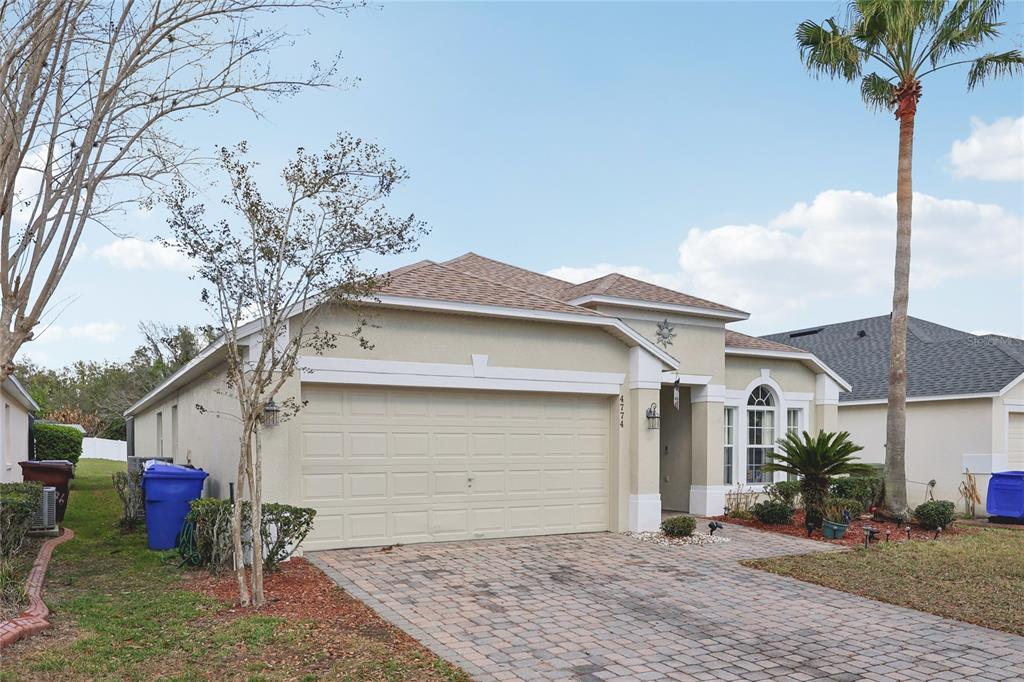 A single-story house with a beige stucco exterior, a two-car garage, and a paver driveway — 4774 CUMBRIAN LAKES DRIVE, KISSIMMEE, FL