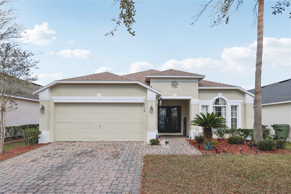 A single-story suburban house with a paved driveway, two-car garage, and a landscaped front yard — 4774 CUMBRIAN LAKES DRIVE, KISSIMMEE, FL