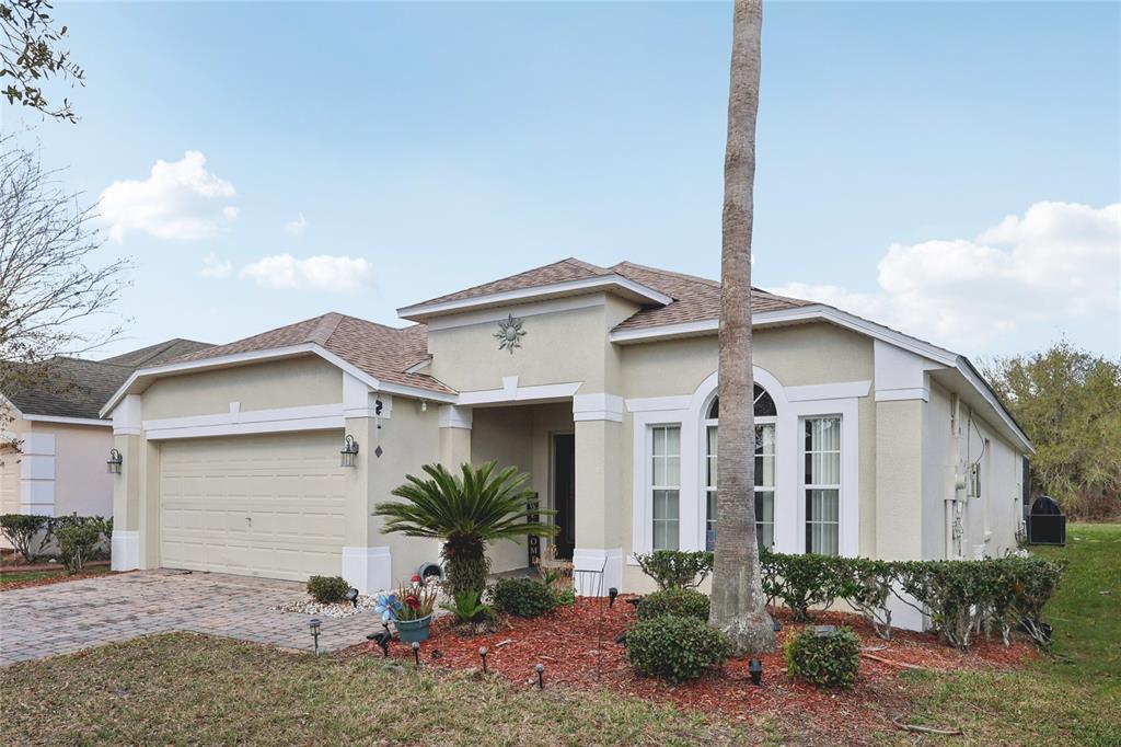 A single-story house with a beige stucco exterior, a two-car garage, and a palm tree — 4774 CUMBRIAN LAKES DRIVE, KISSIMMEE, FL