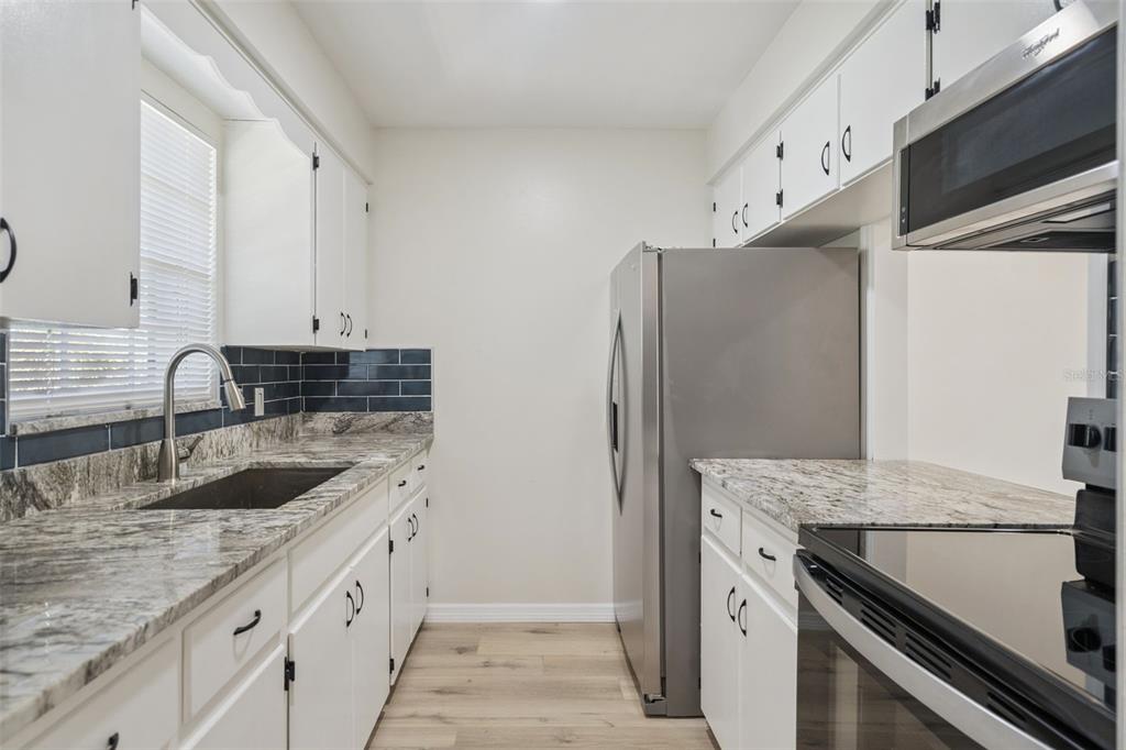 A galley kitchen features white cabinets, granite countertops, stainless steel appliances, and dark blue backsplash tiles — 791 LAKE AVENUE UNIT 5, CLERMONT, FL