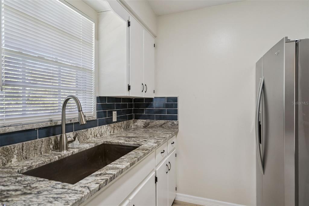 A kitchen features white cabinets, granite countertops, a dark tile backsplash, and a stainless refrigerator — 791 LAKE AVENUE UNIT 5, CLERMONT, FL