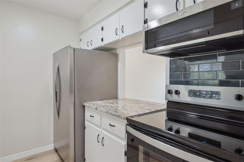 A kitchen features white cabinets, granite countertops, stainless steel appliances, and a dark tile backsplash — 791 LAKE AVENUE UNIT 5, CLERMONT, FL
