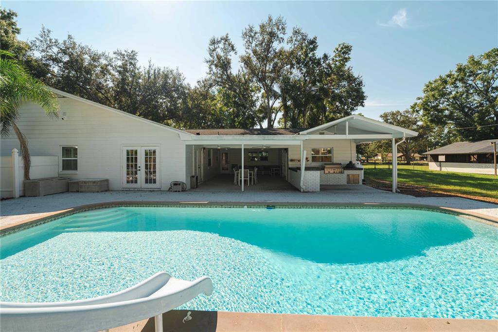 A backyard features a swimming pool with a slide and a covered patio area — 15509 CASEY ROAD, TAMPA, FL