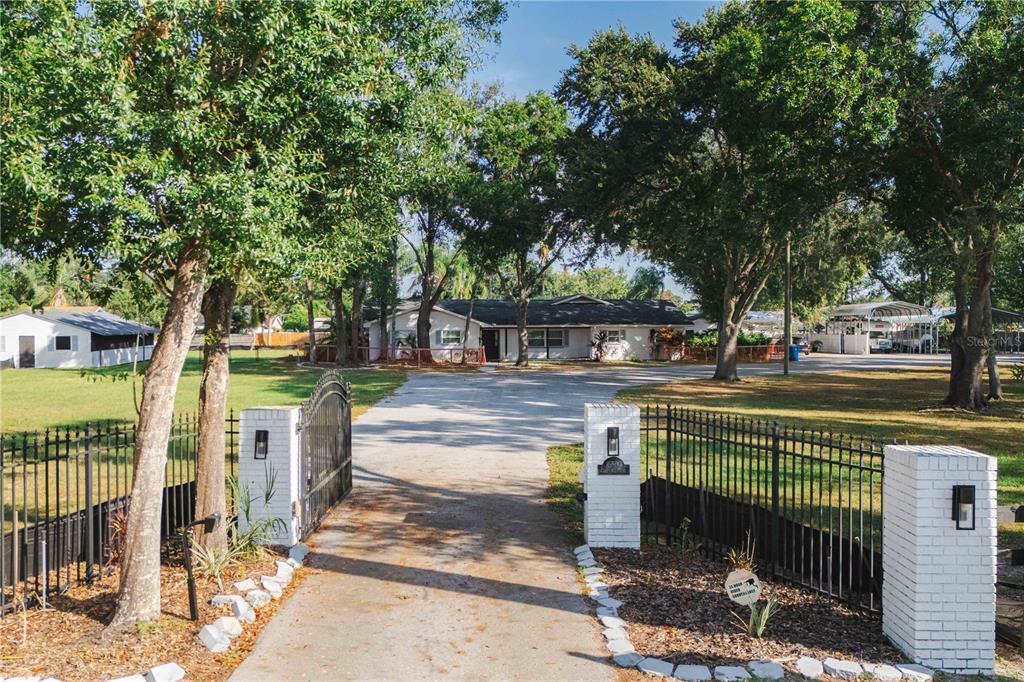 A gated driveway leads to a single-story house surrounded by trees and a grassy lawn — 15509 CASEY ROAD, TAMPA, FL