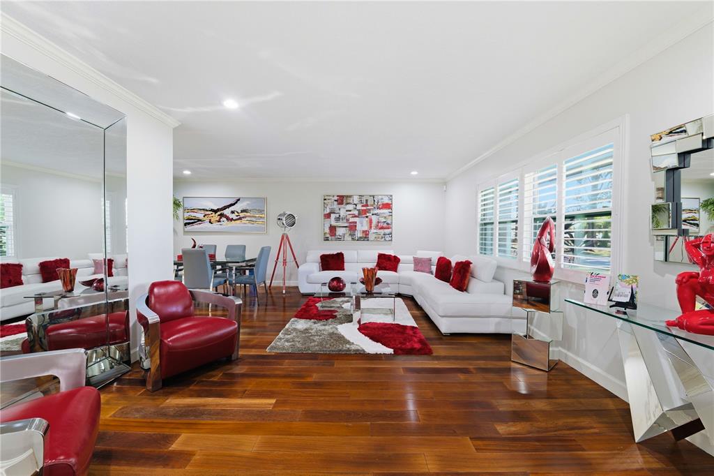 A living room with white sectional sofas, red accents, hardwood floors, and a large mirror — 15509 CASEY ROAD, TAMPA, FL