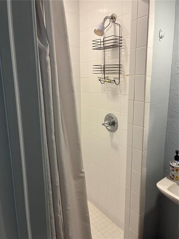 A tiled shower stall features a hanging metal caddy and a silver shower head — 407 N SHINE AVENUE, ORLANDO, FL