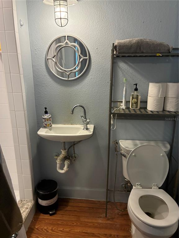A small bathroom features a wall-mounted sink, a toilet, and a metal shelving unit — 407 N SHINE AVENUE, ORLANDO, FL