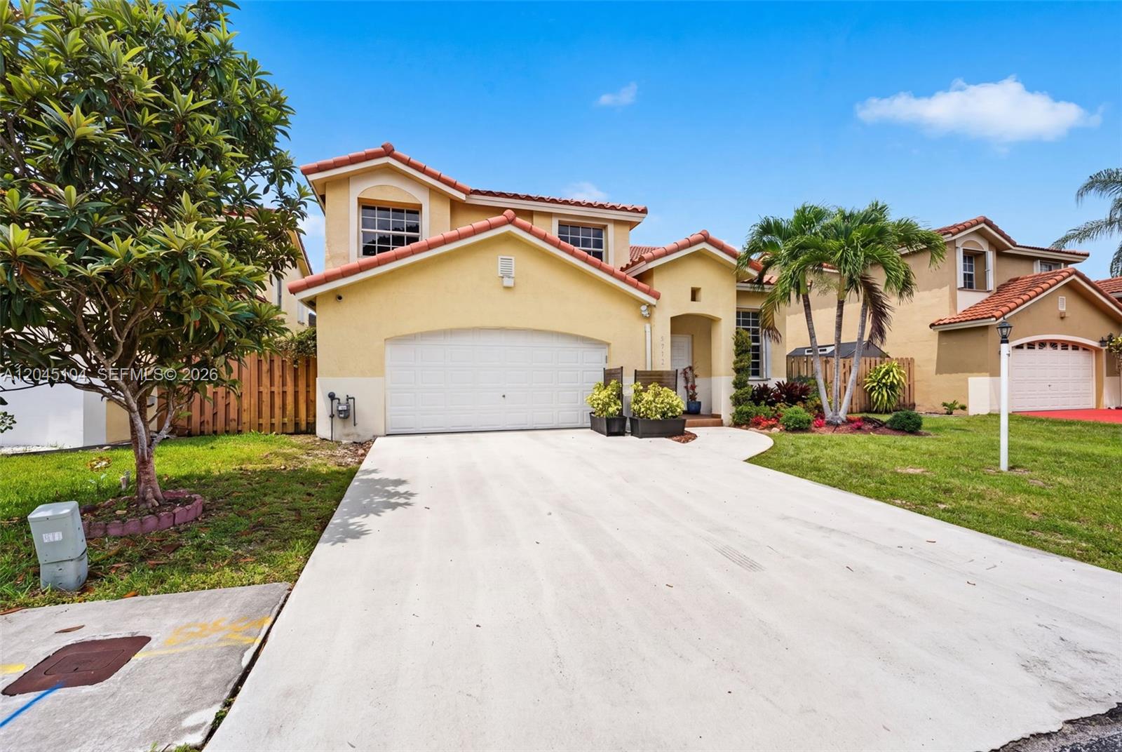 A two-story yellow stucco house features a tile roof, a garage, and a concrete driveway — 15602 SW 109th Ter, Miami FL 33196, MIAMI, FL