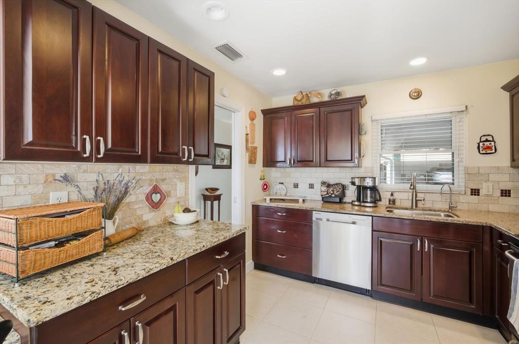 A kitchen features dark wood cabinets, granite countertops, a stainless steel dishwasher, and tile backsplash — 2320 AQUABLUFF PLACE UNIT V274, SARASOTA, FL