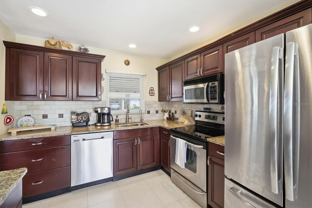 A kitchen with dark wood cabinets, granite countertops, and stainless steel appliances — 2320 AQUABLUFF PLACE UNIT V274, SARASOTA, FL