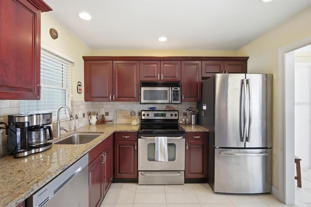A kitchen features dark wood cabinets, stainless steel appliances, granite countertops, and a tile backsplash — 2320 AQUABLUFF PLACE UNIT V274, SARASOTA, FL