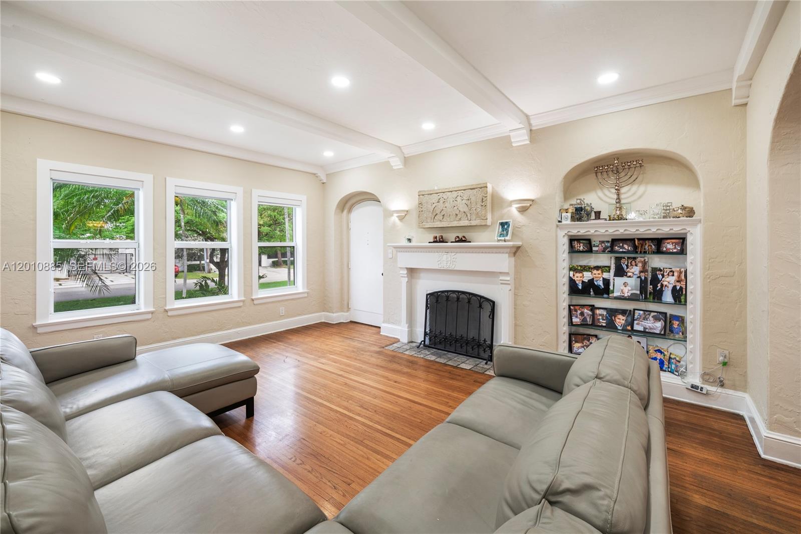 A living room features hardwood floors, a fireplace, built-in shelving, and light-colored leather sofas — 4501 Prairie Ave # 1, Miami Beach FL 33140, MIAMI BEACH, FL