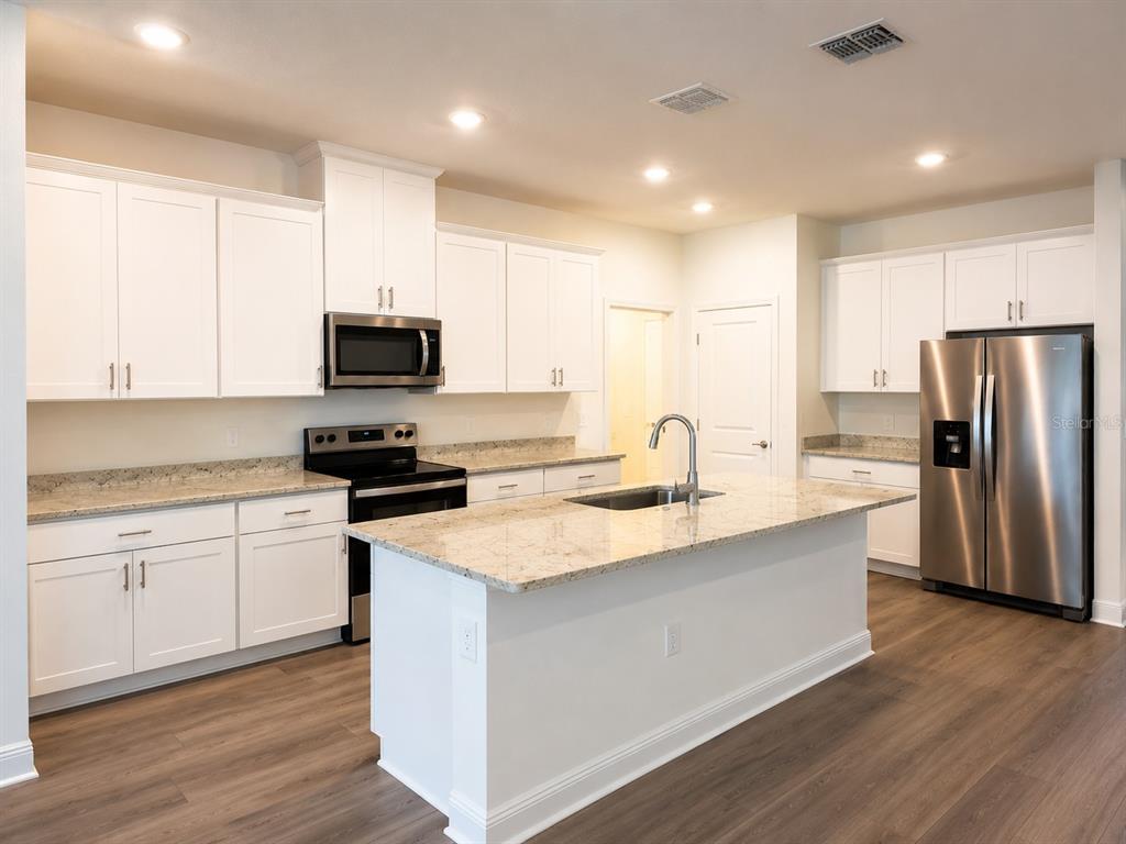 A kitchen features white cabinets, granite countertops, stainless steel appliances, and wood-look flooring — 1789 ARCHER DRIVE, MINNEOLA, FL