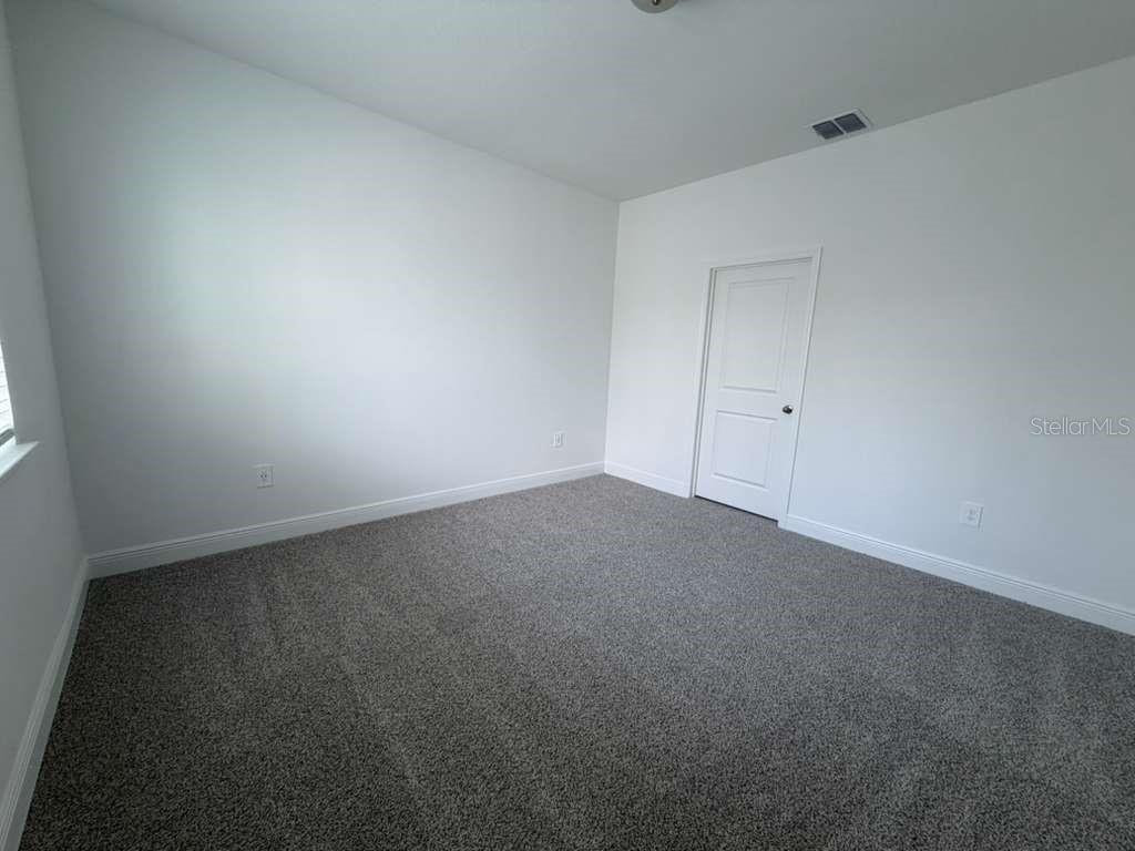 An empty bedroom features gray carpet, white walls, and a single white door — 1789 ARCHER DRIVE, MINNEOLA, FL