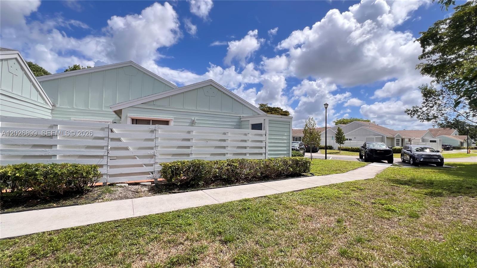 A light green house with a white wooden fence sits beside a paved sidewalk — 13775 SW 149th Cir Ln # 86, Miami FL 33186, MIAMI, FL