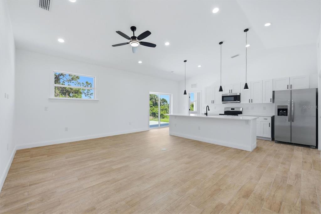 A bright, open-concept kitchen and living area featuring white cabinetry, stainless appliances, and wood-look flooring — 6 BANK COURT, PLACIDA, FL