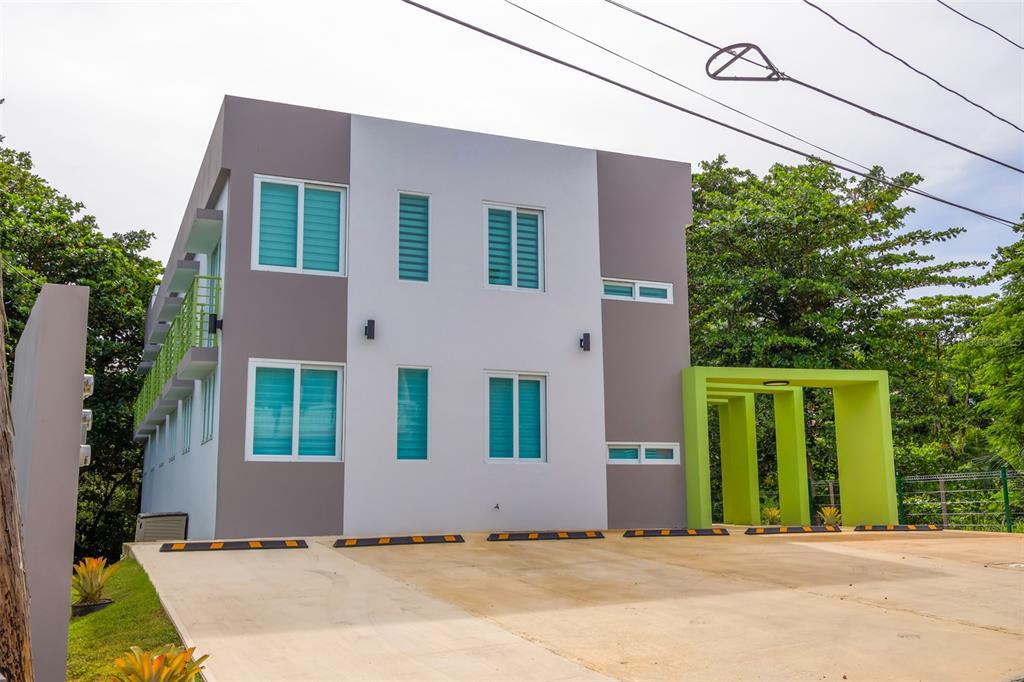 A modern three-story apartment building with a concrete parking lot and a green entrance structure — Km 4.7 CARR 413 INT UNIT 102, RINCON, PR