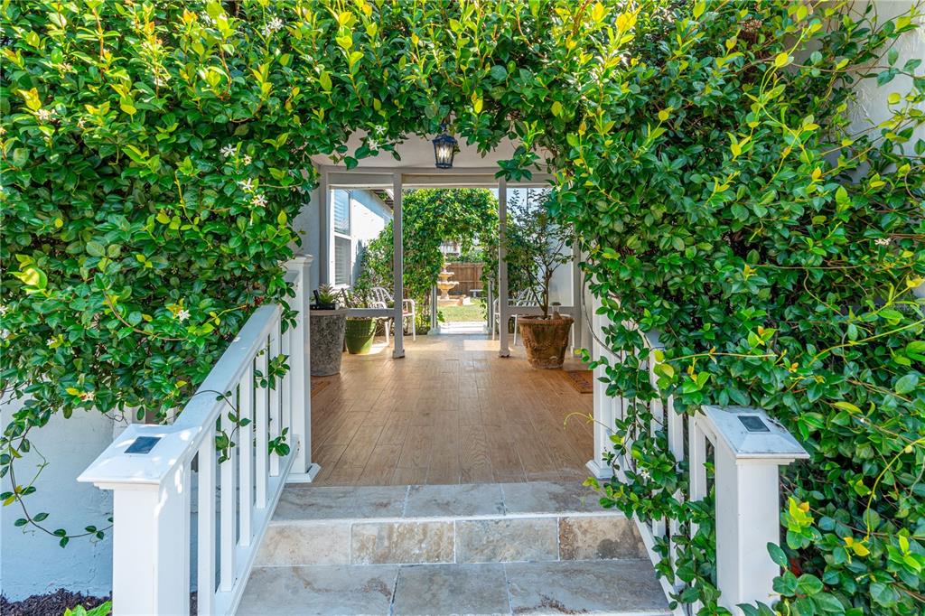 A covered porch with tiled steps and flooring is framed by lush green climbing vines — 129 ROSALYN AVENUE, DAYTONA BEACH, FL