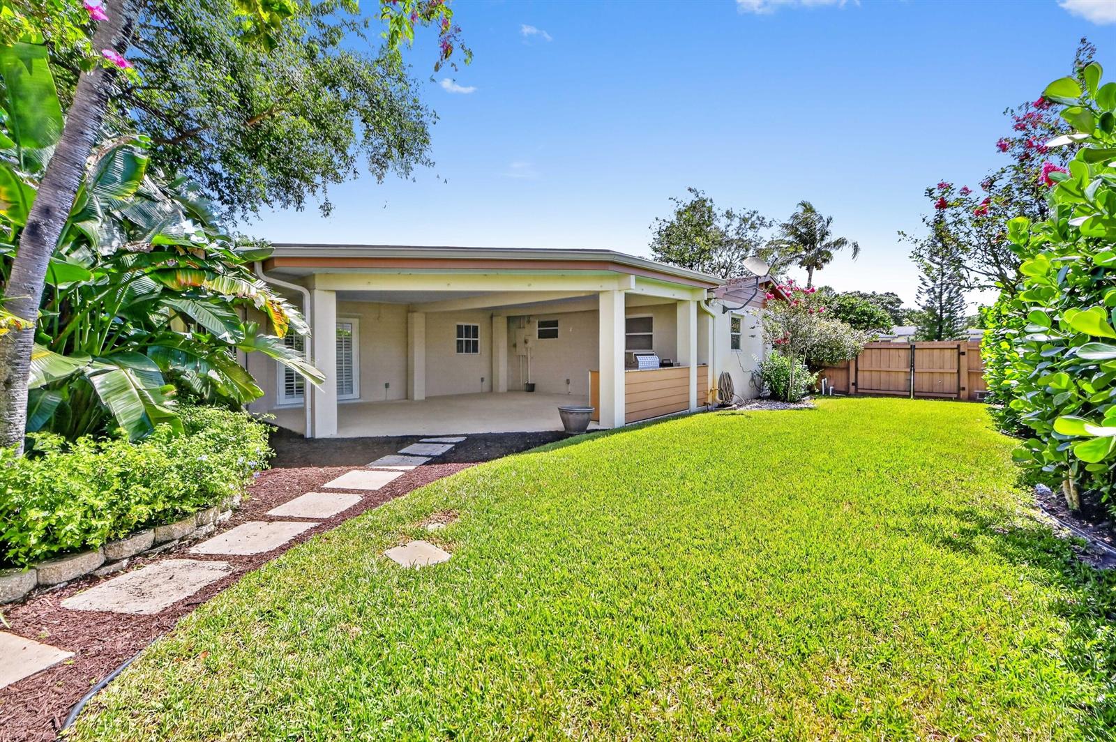 A covered patio overlooks a grassy backyard with a stone walkway and lush landscaping — 313 Poe Drive, Palm Springs FL 33461, PALM SPRINGS, FL